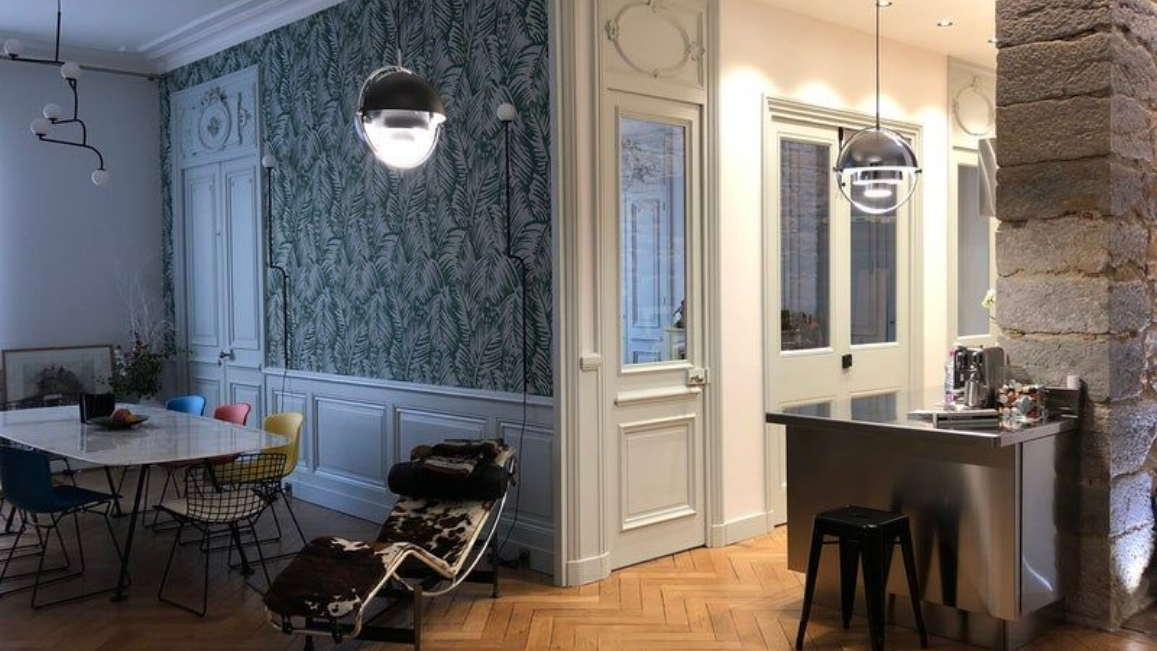 Intérieur d'appartement élégant : coin repas avec table en marbre, mur tapissé, cuisine avec îlot en acier inoxydable.