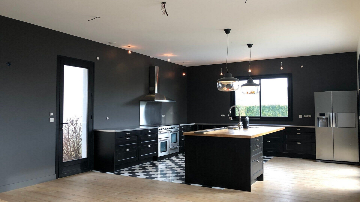 Cuisine noire moderne avec électroménagers en acier inoxydable, îlot et grande fenêtre.