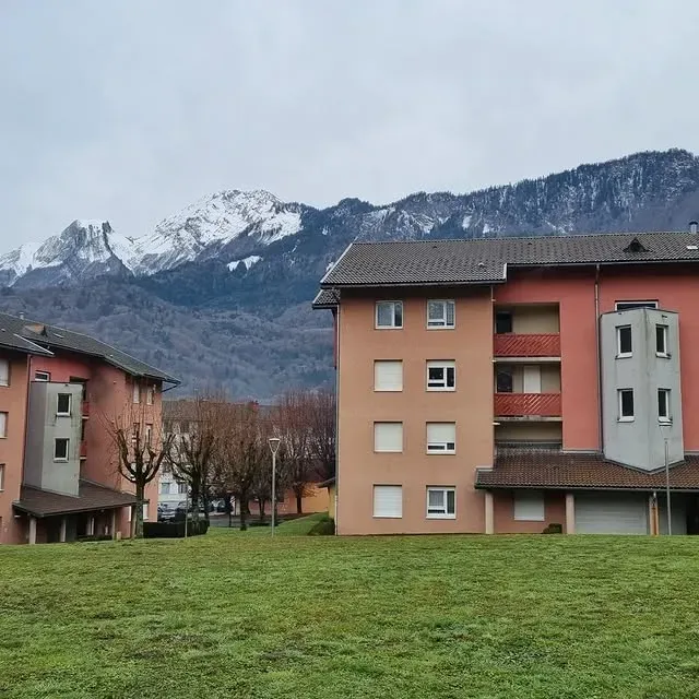 Immeubles d'habitation avec arrière-plan montagneux ; pelouse verte, ciel couvert.