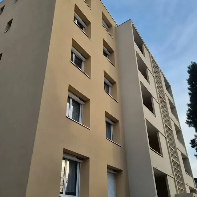 Immeuble d'appartements beige avec balcons, fenêtres et ciel bleu.