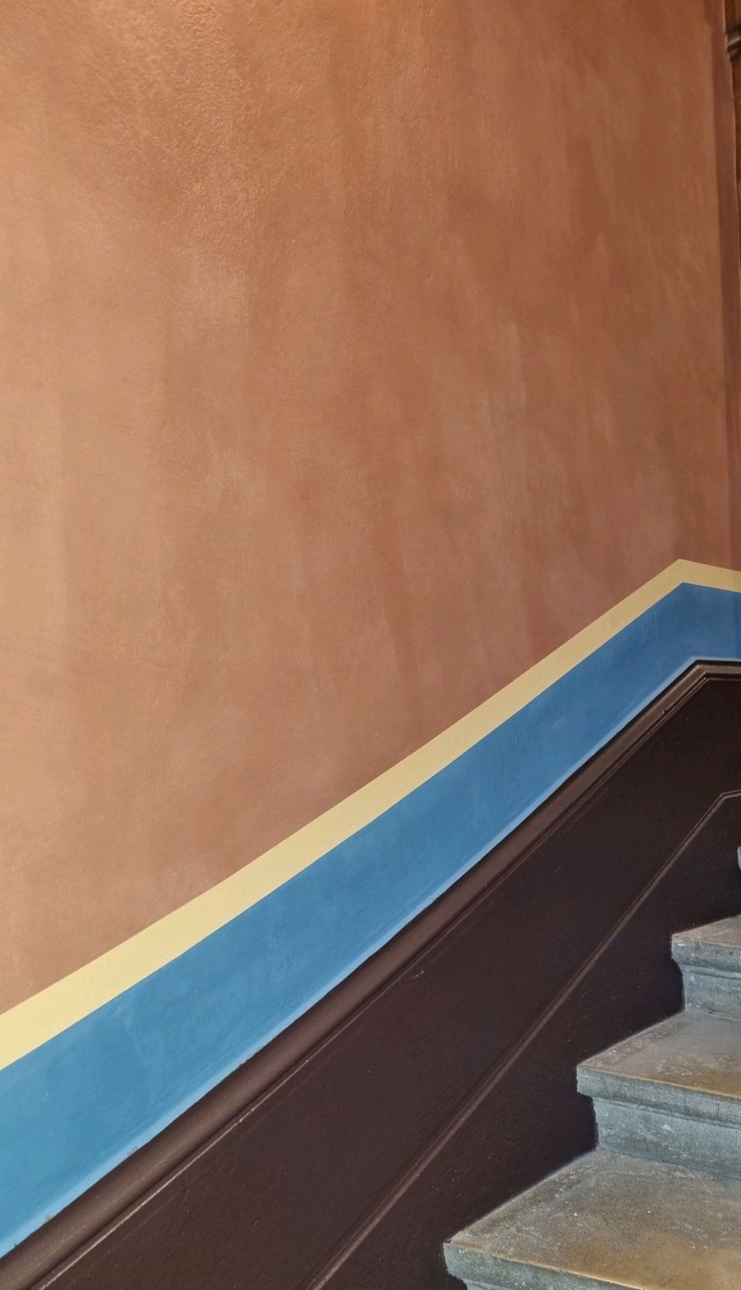 Mur couleur terre cuite finition badigeon à la chaux avec des bordures bleues et jaunes.