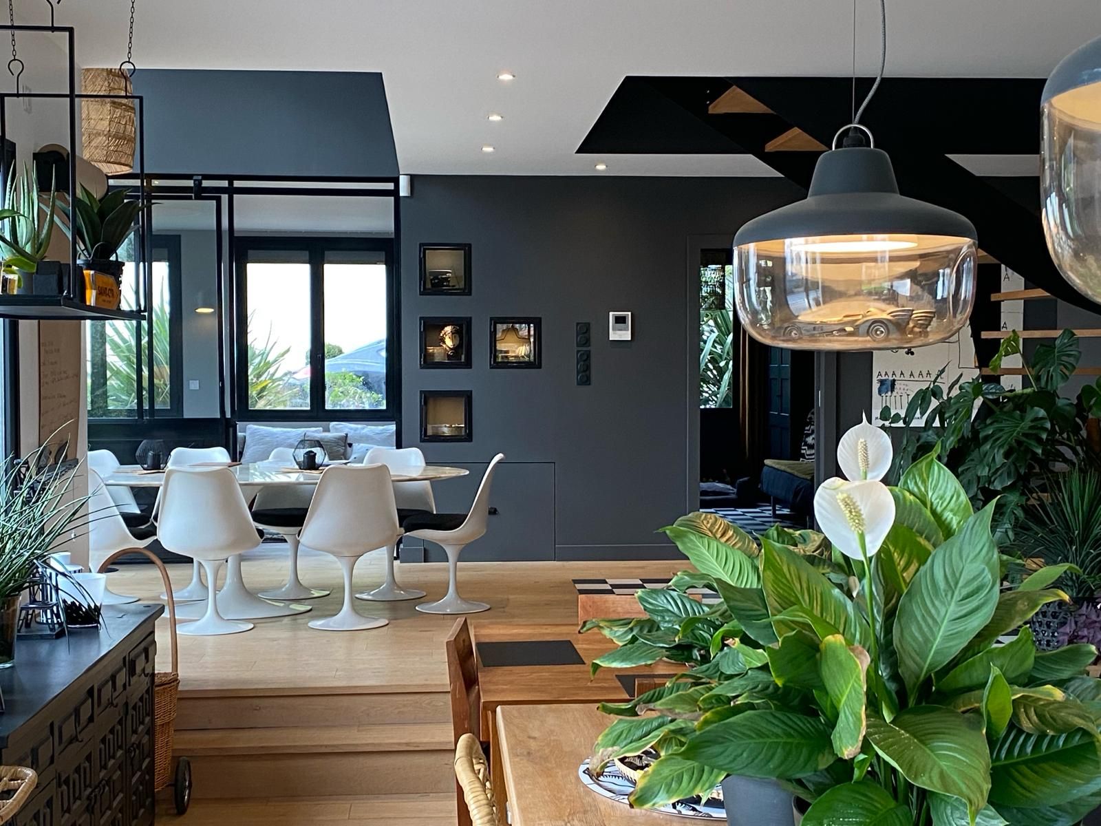 Salle à manger moderne avec chaises blanches, murs gris foncé et une grande plante.
