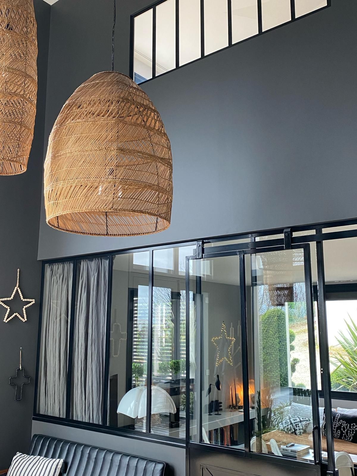 Des lampes en osier suspendues dans une pièce moderne aux murs gris foncé et à la cloison vitrée.