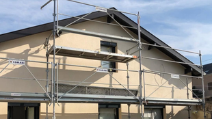 Échafaudage contre une maison pour travaux extérieurs ; murs beiges, toit foncé.