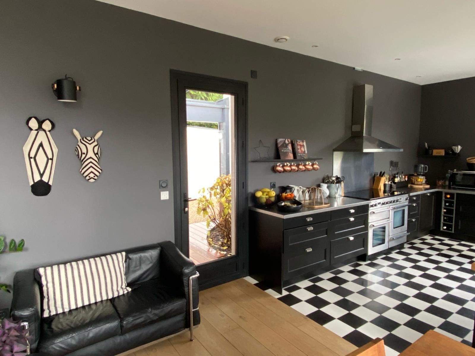Cuisine avec placards noirs, sol à damier, murs gris foncé, décorations zébrées et canapé noir.