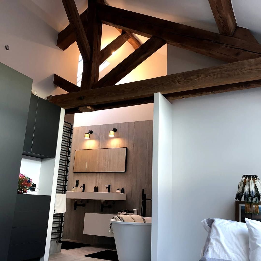 Salle de bains avec poutres apparentes, murs blancs et baignoire autoportante.