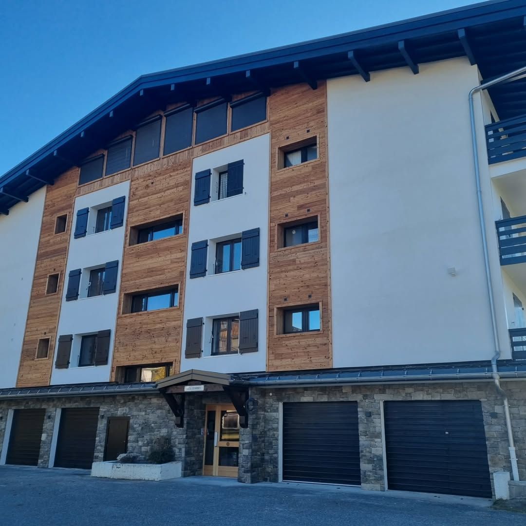 Vue extérieure d'un immeuble d'appartements de style alpin avec une façade en bois et blanche.