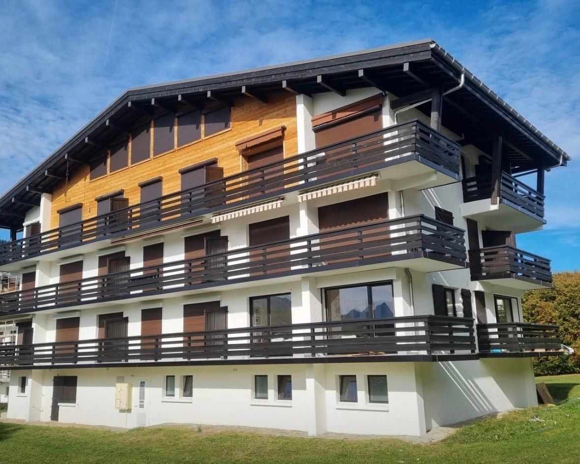 Petit bâtiment de couleur crème avec un toit en tuiles de terre cuite, deux fenêtres, posé sur du gravier, sous un ciel bleu.