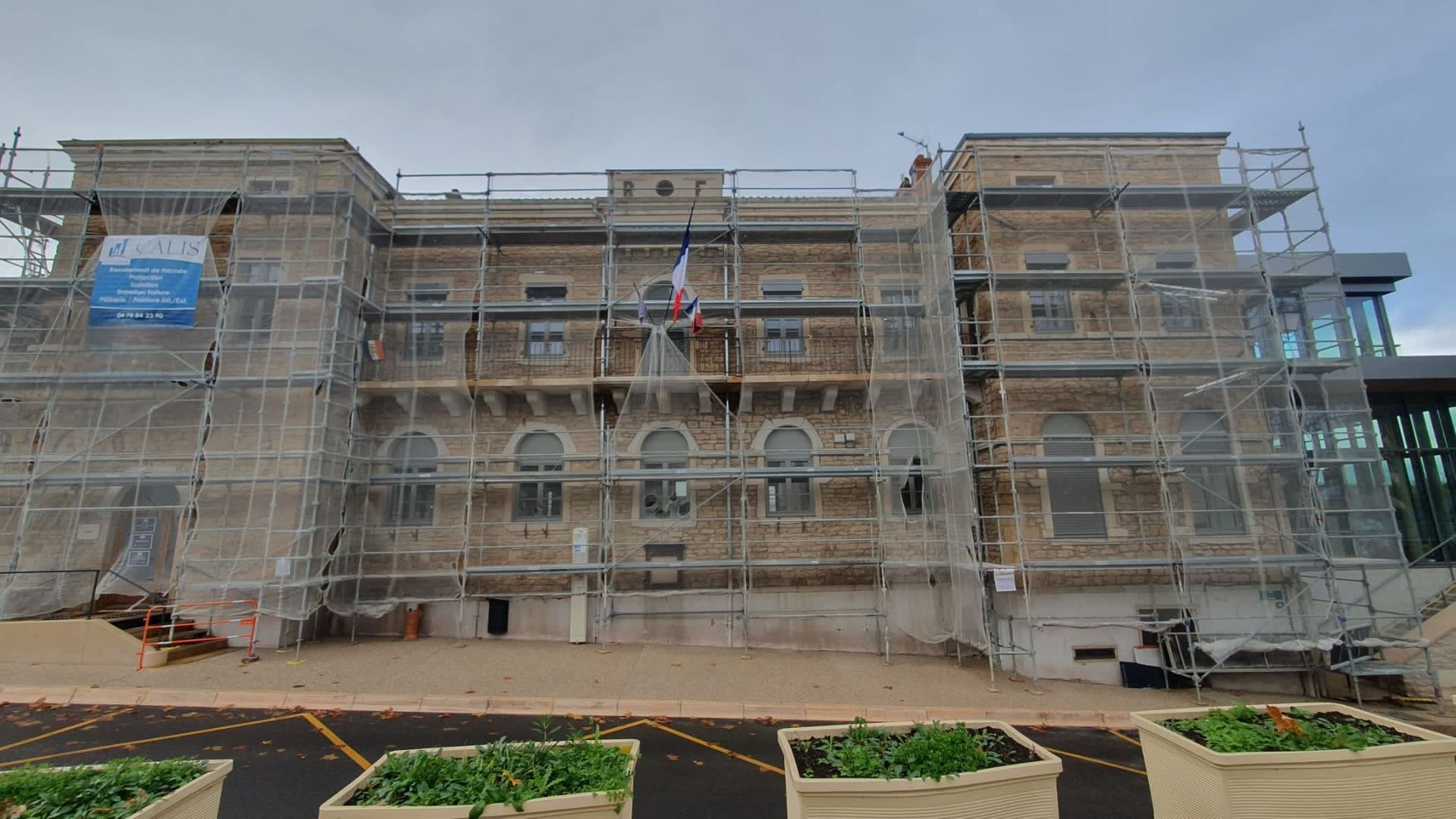 Échafaudage contre une maison pour travaux extérieurs ; murs beiges, toit foncé.