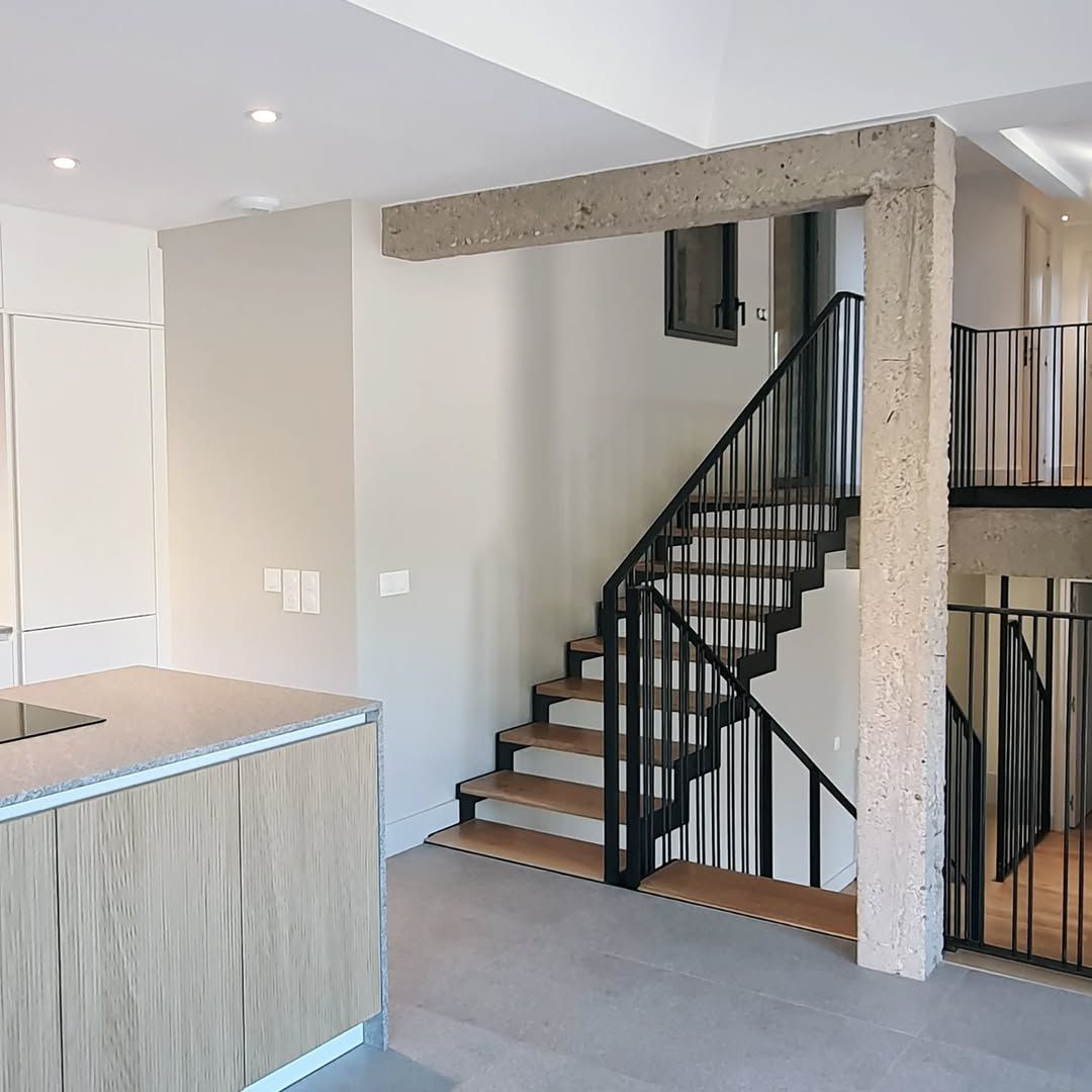 Vue intérieure d'une maison moderne avec un escalier, une poutre en béton et des accents en bois.