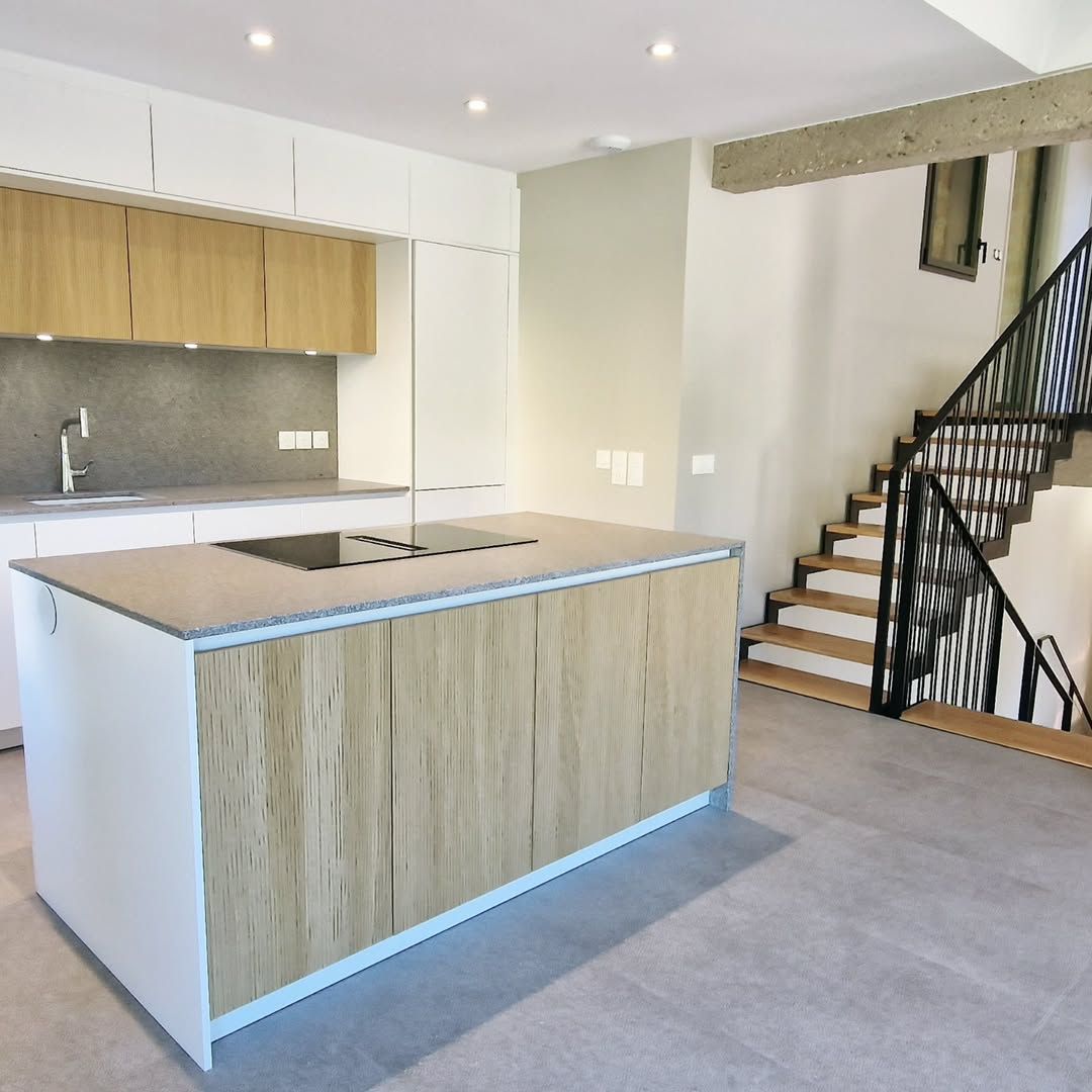 Cuisine moderne avec îlot central, armoires en bois et escalier.