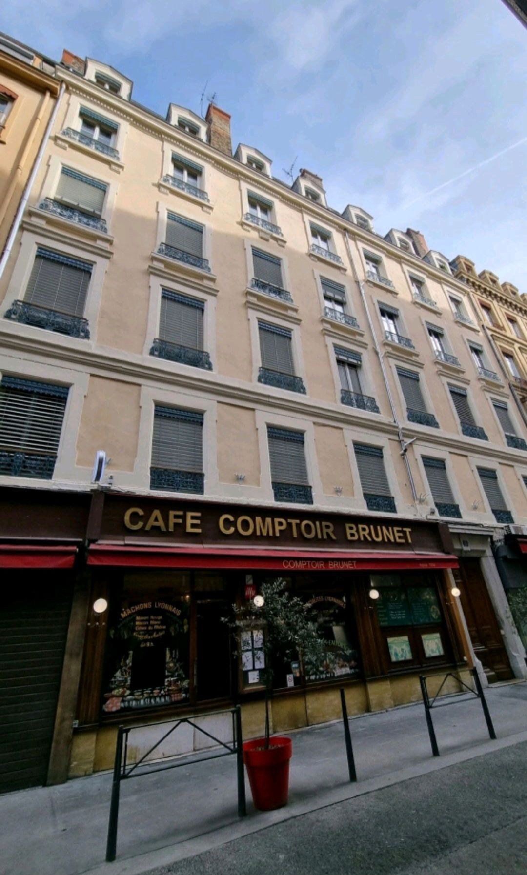 Vue extérieure du Café Comptoir Brunet dans un immeuble à plusieurs étages aux volets fermés.