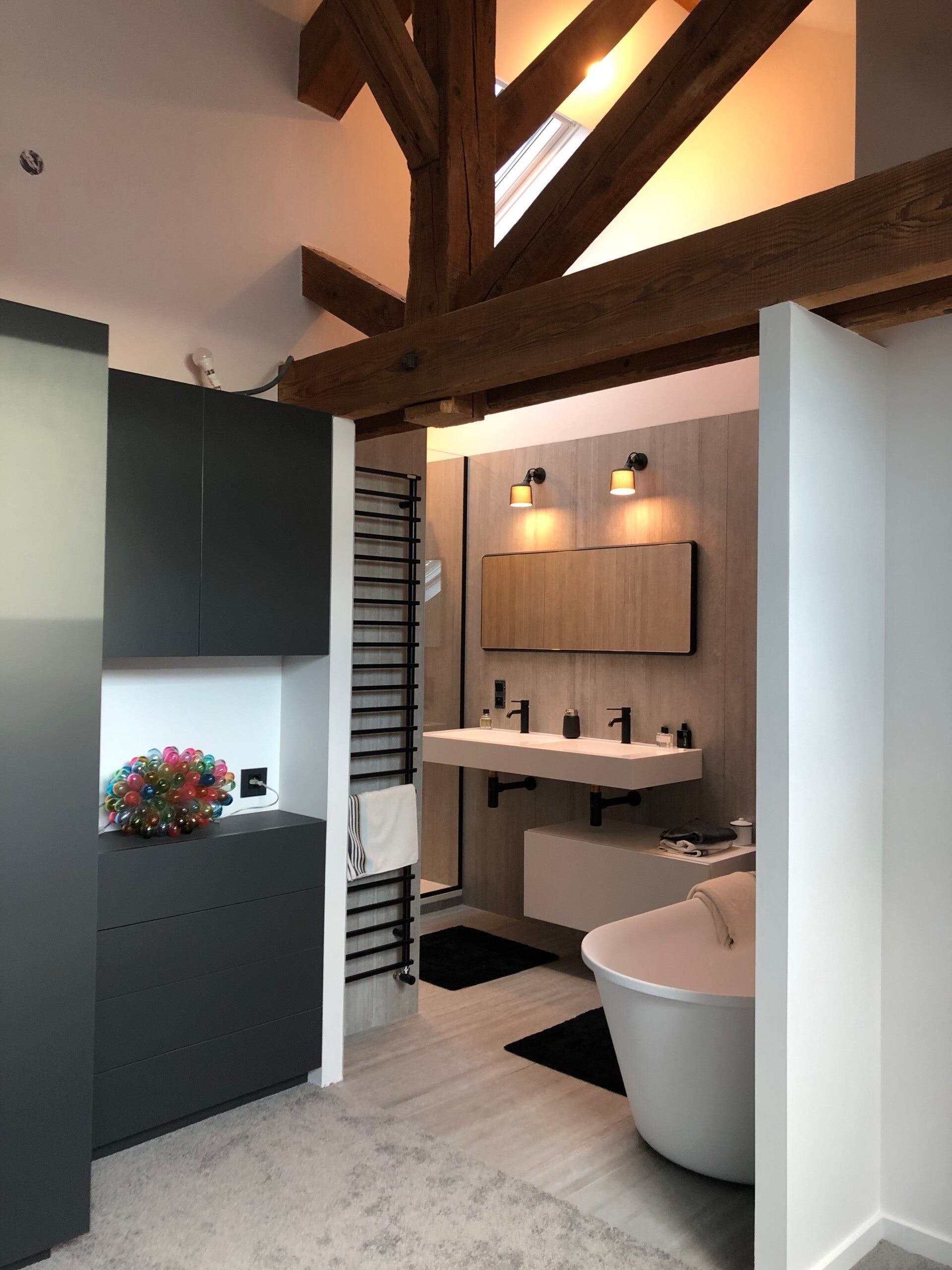 Salle de bains moderne avec armoires noires, murs blancs, accents de bois et baignoire autoportante.