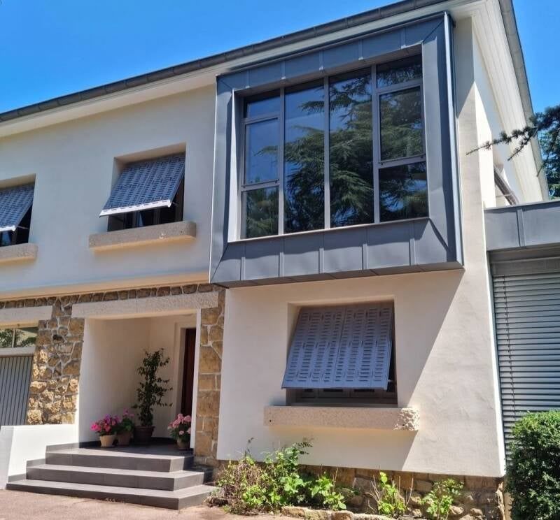 Maison blanche à deux étages avec encadrements de fenêtres et auvents gris.