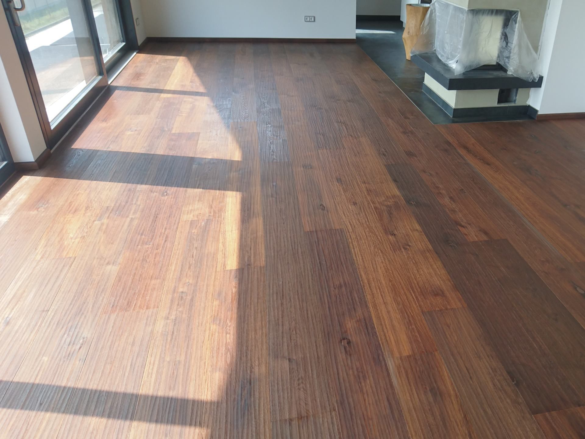 Dunkelbrauner Holzparkettboden in einem hellen, modernen Raum neben einer Glasschiebetür.