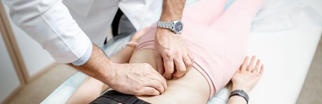 Un médico está examinando el estómago de una mujer en una mesa.