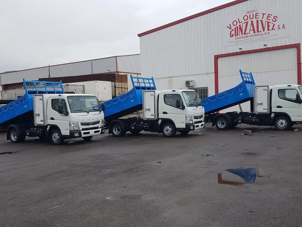 Tres camiones de volteo están estacionados frente a un edificio que dice Gonzalo.