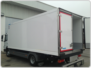 Un camión blanco con las puertas abiertas está estacionado frente a un edificio.