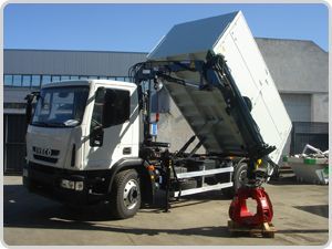 Un camión volquete con una grúa acoplada está estacionado frente a un edificio.