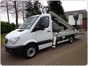 Una camioneta blanca con una grúa en la parte trasera está estacionada en un camino de entrada de ladrillos.