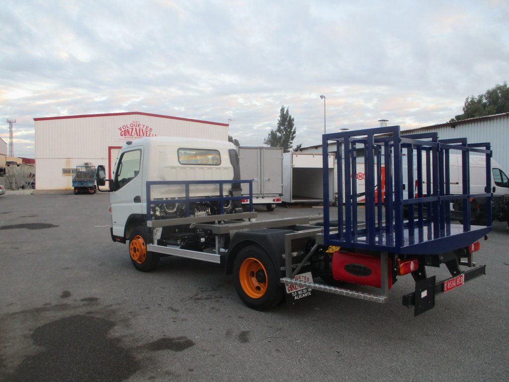 Un camión blanco con una plataforma azul en la parte trasera está estacionado en un estacionamiento.