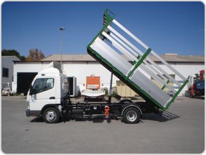 Un camión volquete blanco y verde está estacionado frente a un edificio.