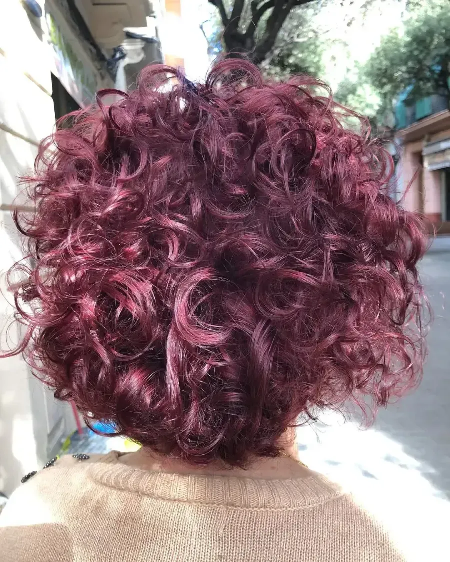 Espalda de una persona con cabello corto y rizado color burdeos de pie al aire libre en una acera.