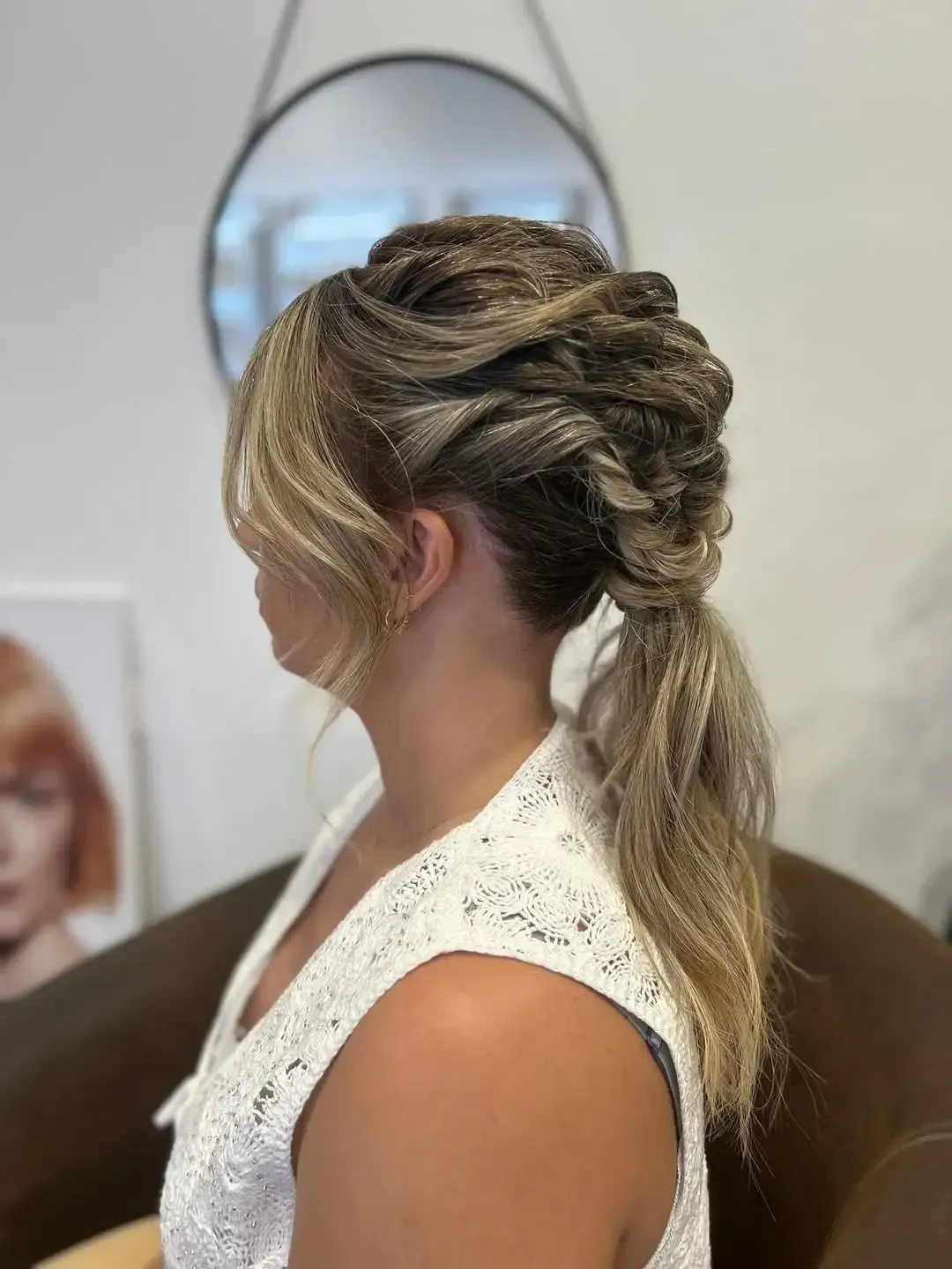 Recogido rubio trenzado con coleta baja, visto de perfil en interiores.