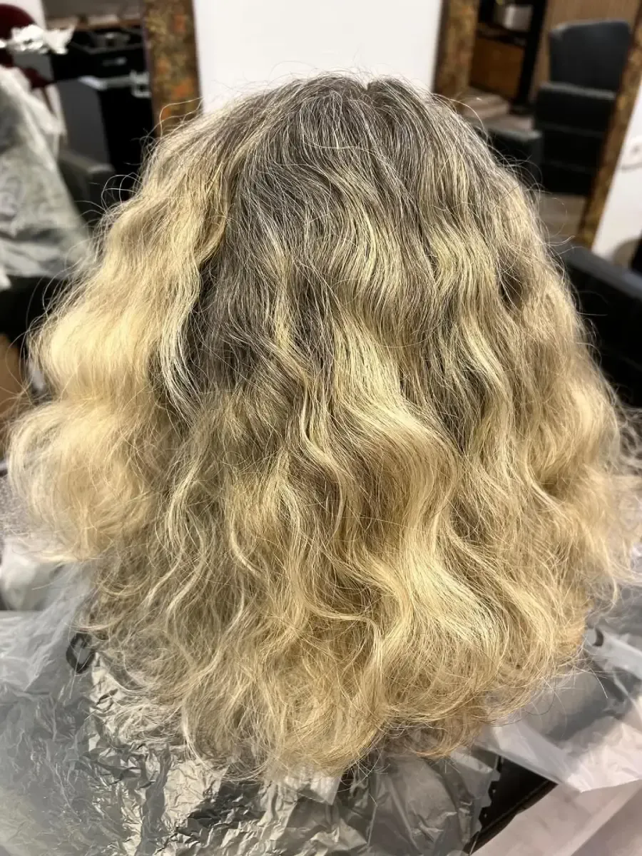 Corte de pelo corto, gris plateado y capeado, en una peluquería, vista lateral, en una persona sentada con una capa negra.