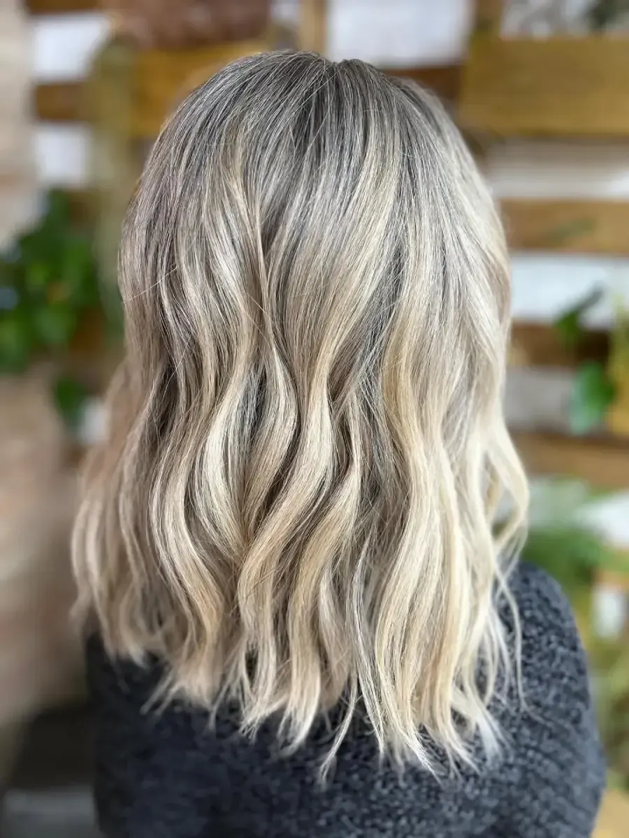 Persona con cabello corto color lavanda en una peluquería, mostrada de perfil con una leve sonrisa.