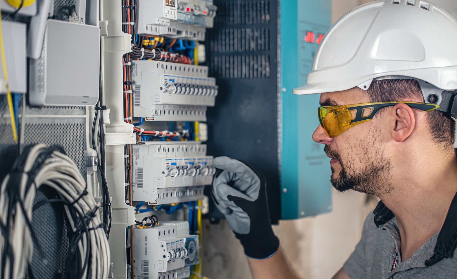 Electricista con casco y gafas de seguridad trabajando en un panel de disyuntores.