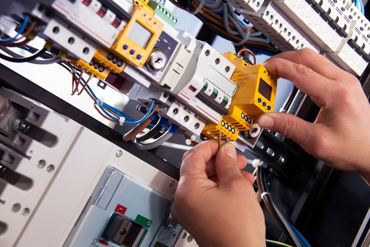 Manos cableando componentes eléctricos dentro de un panel; cables de varios colores y disyuntores visibles.