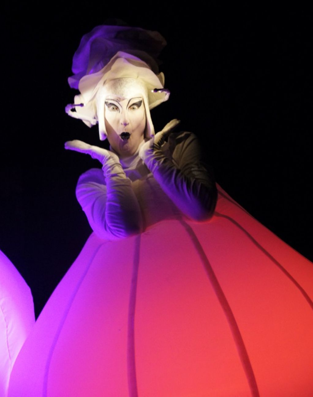 Una mujer con un vestido rojo y morado está parada en la oscuridad.