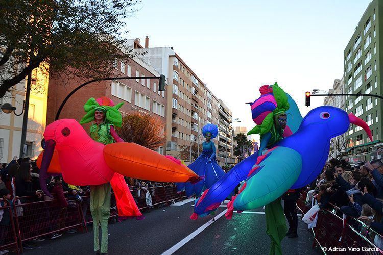 Un grupo de personas caminando por una calle con pájaros inflables de colores.