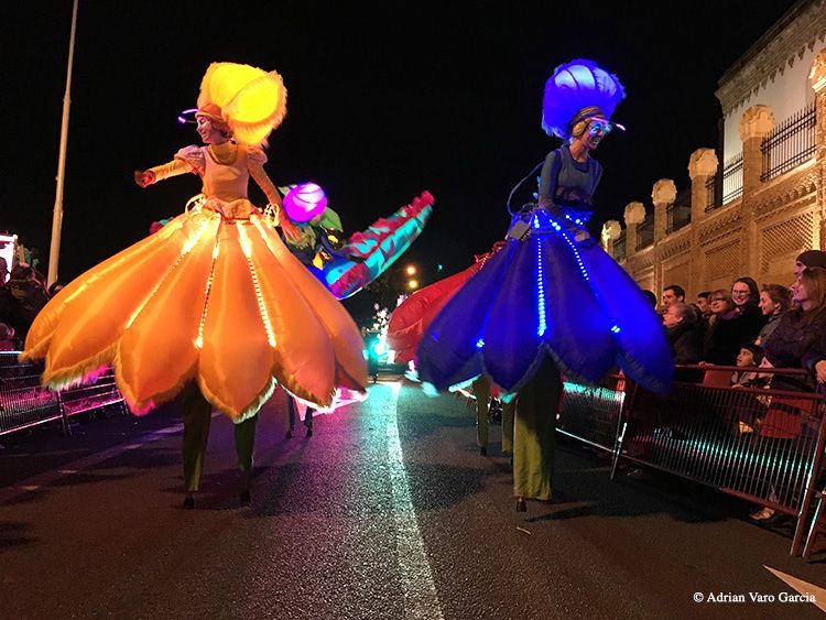 Dos mujeres caminan sobre zancos en un desfile nocturno.
