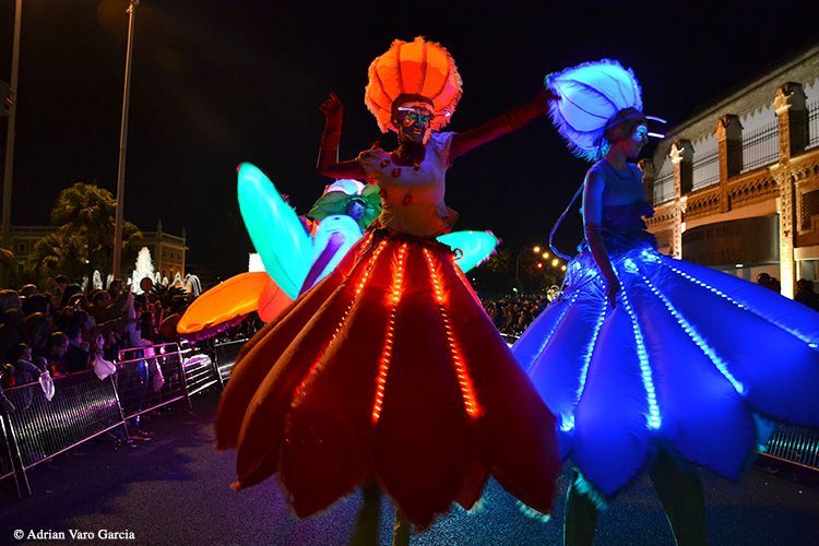Una pareja de personas de pie sobre zancos con luces en sus vestidos.
