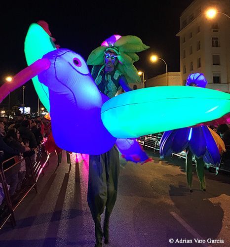 Una persona en zancos sosteniendo un colibrí que brilla en la oscuridad
