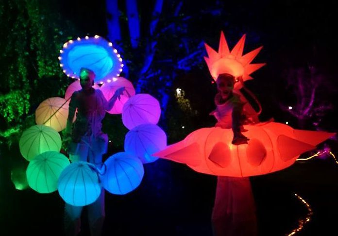 Dos personas de pie sobre zancos con linternas brillantes a su alrededor.