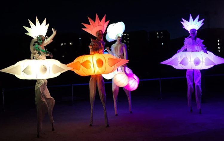 Un grupo de personas de pie sobre zancos con luces en sus cabezas.