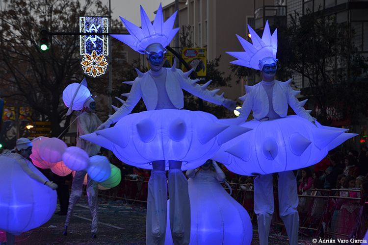 Un grupo de personas de pie sobre zancos con paraguas azules.