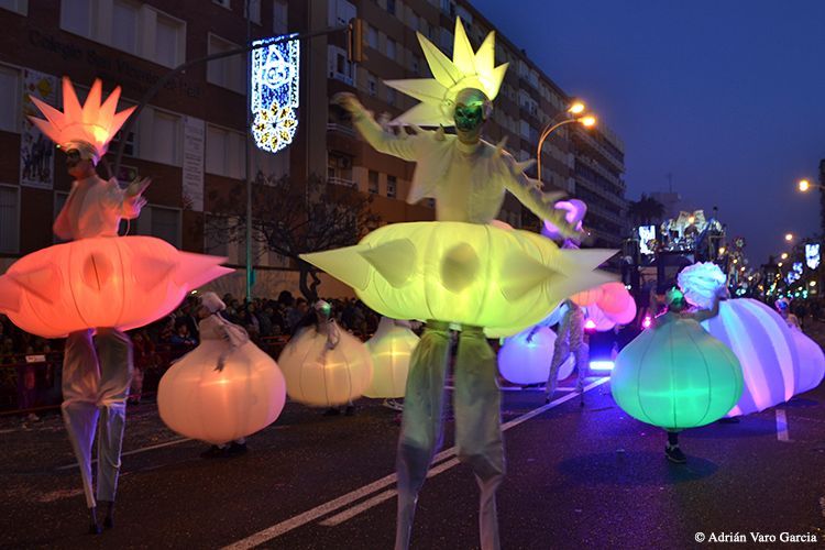 Un grupo de personas camina por una calle con linternas brillantes sobre zancos.
