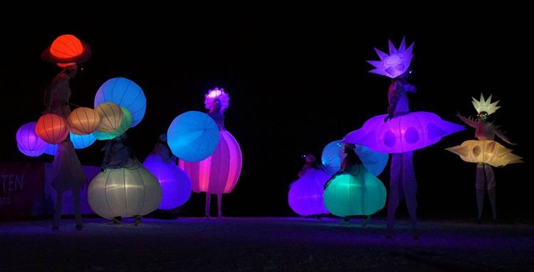 Un grupo de personas de pie sobre zancos con linternas que brillan en la oscuridad.