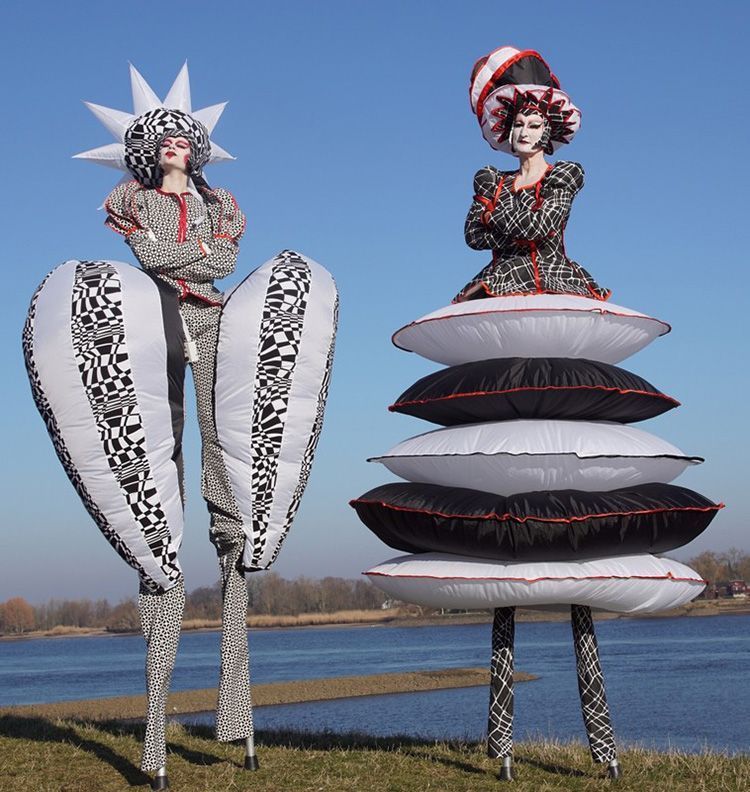 Dos personas en zancos están de pie junto a una pila de almohadas.