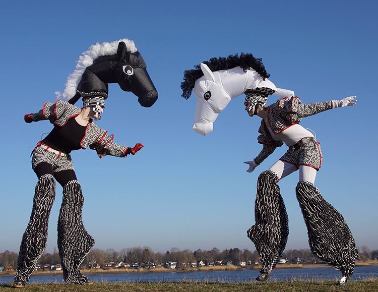 Dos personas de pie sobre zancos con cabezas de caballo sobre sus cabezas