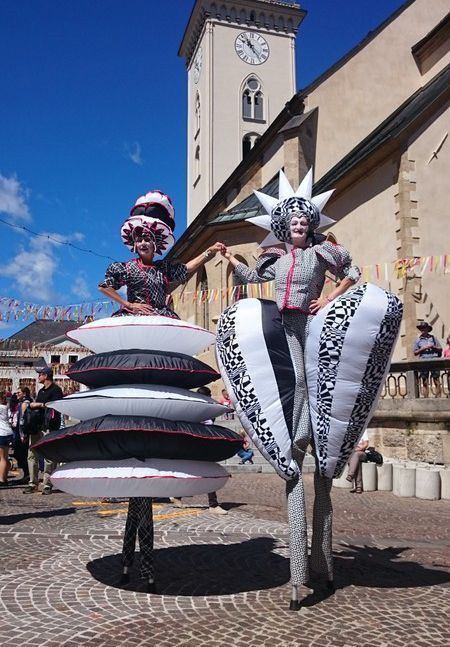 Un par de personas paradas sobre zancos sosteniendo almohadas frente a un edificio.