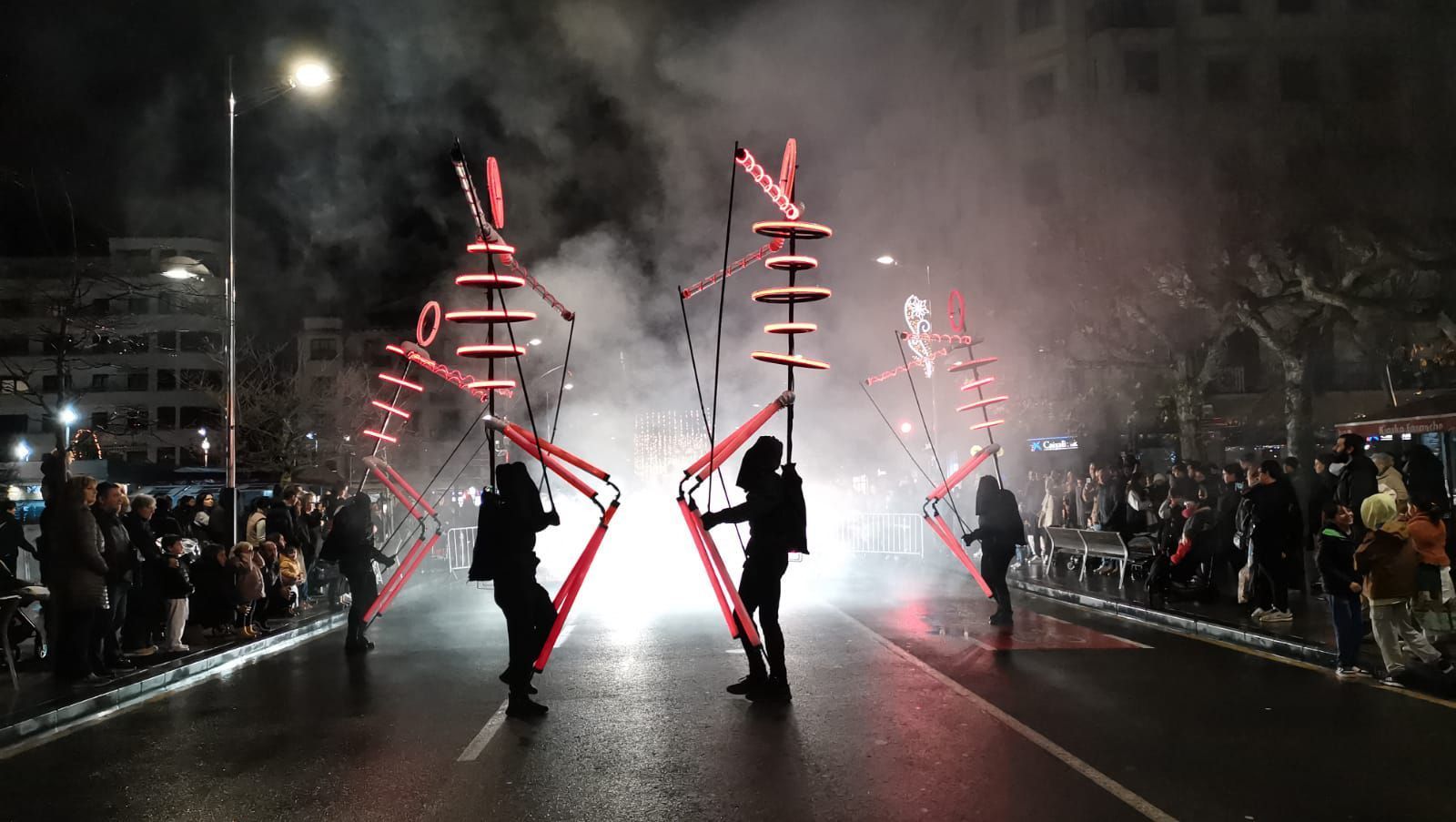 Un grupo de personas camina por una calle con fuegos artificiales de fondo.