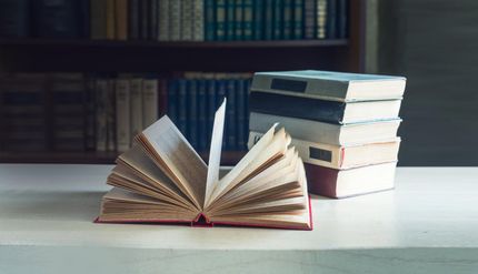 Un libro abierto está sobre una mesa al lado de una pila de libros.