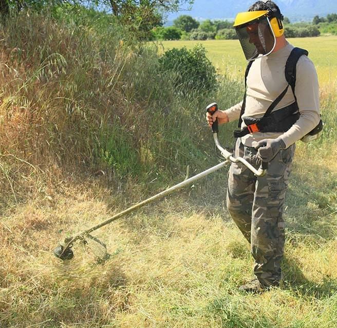 Homme débroussaillant un talus aux herbes hautes