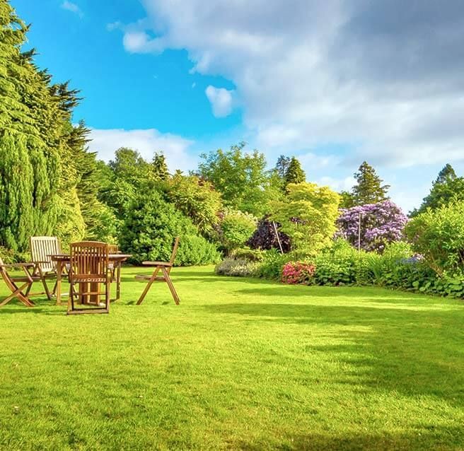 Table et chaises disposées dans un jardin entouré d'arbres et de plantes