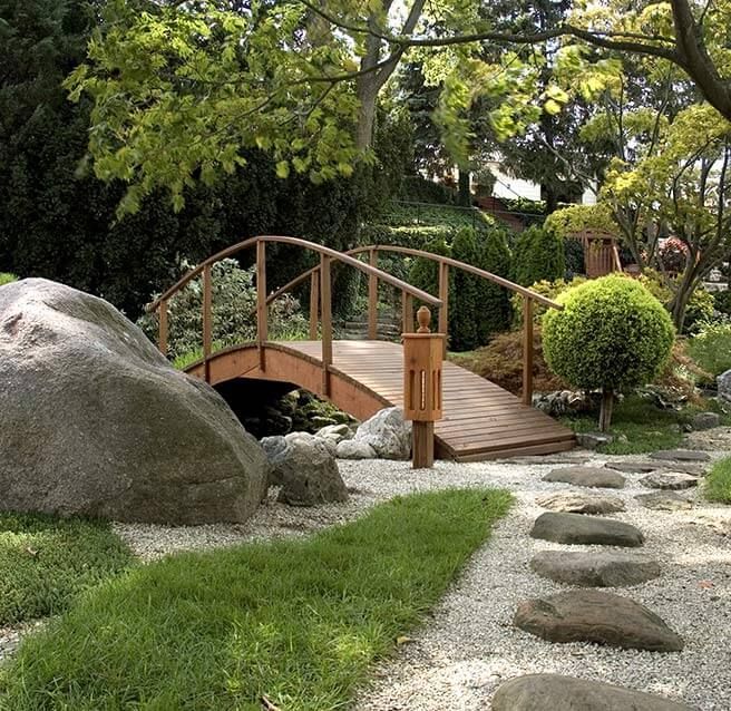 Jardin avec pont, sentier de gravier et arbustes taillés